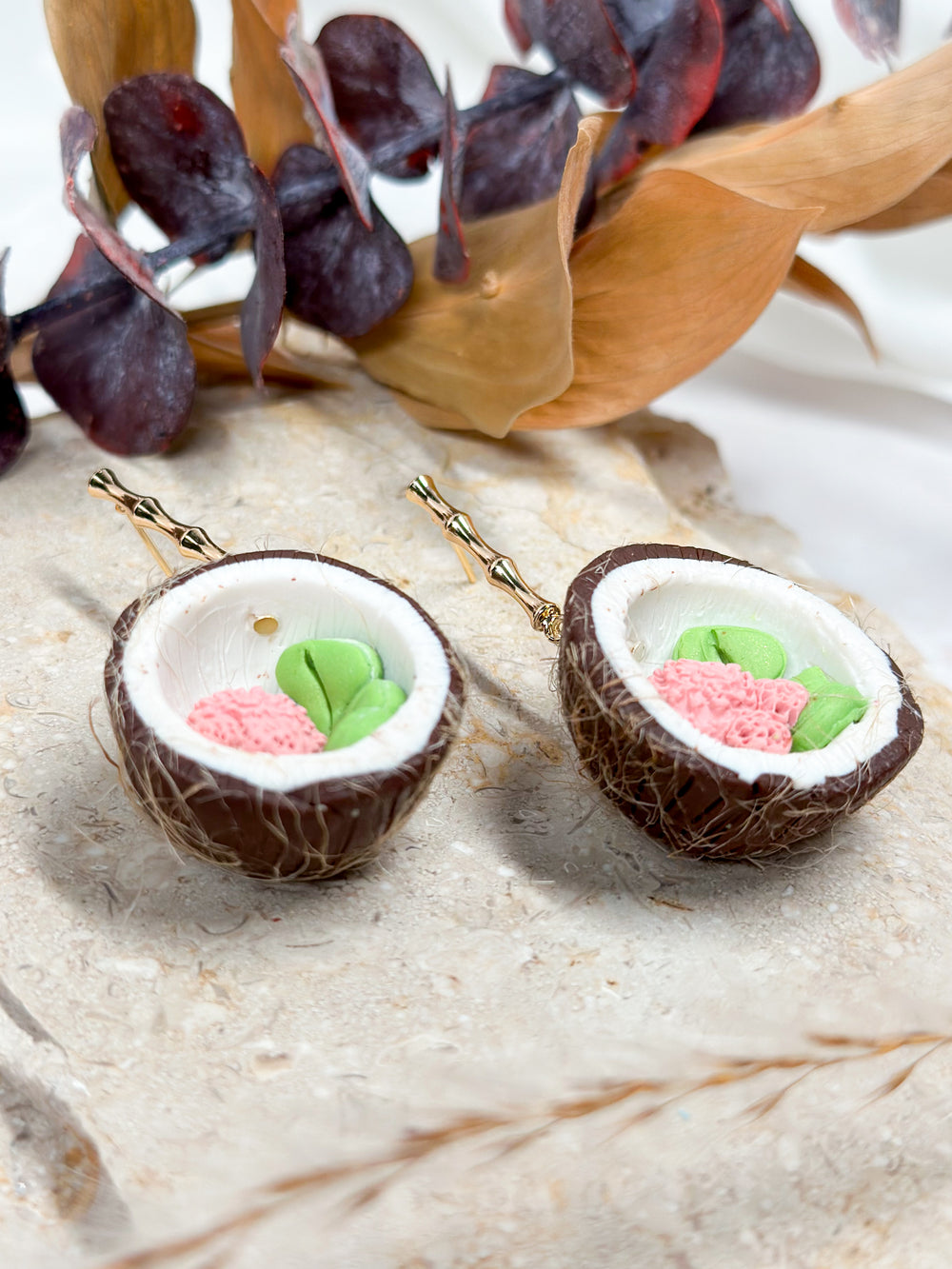 The Dappled Wood's Devi earring, which are coconuts with a pink flower and monstera leaf inside, on gold bamboo posts. Hypoallergenic for sensitive ears.