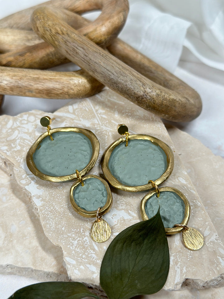 Matte dimpled circle earrings with gold trim, featuring a modern organic shape and soft green hue. Handmade statement jewelry for summer 2024 from The Dappled Wood.