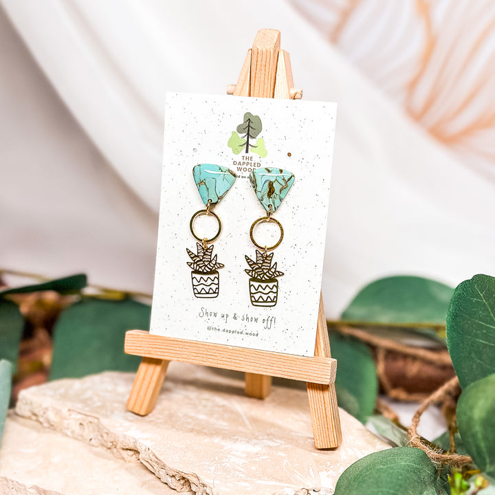 The Dappled Wood Dusty Turquoise earrings, featuring handcrafted faux stone polymer clay tops in a marbled turquoise pattern with brass succulent charms. Set on 18k gold-filled posts for a nature-inspired, lightweight statement look.