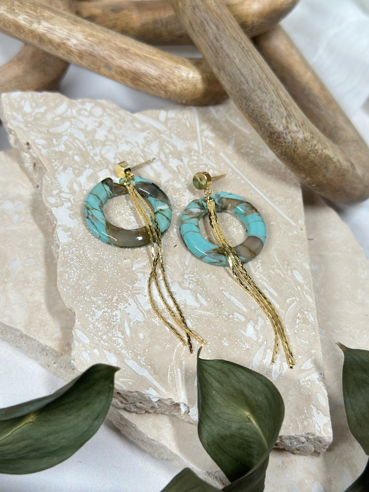 A variation of Dusty Turquoise earrings featuring circular faux stone elements with gold chain tassels. Handmade statement jewelry for summer 2024.