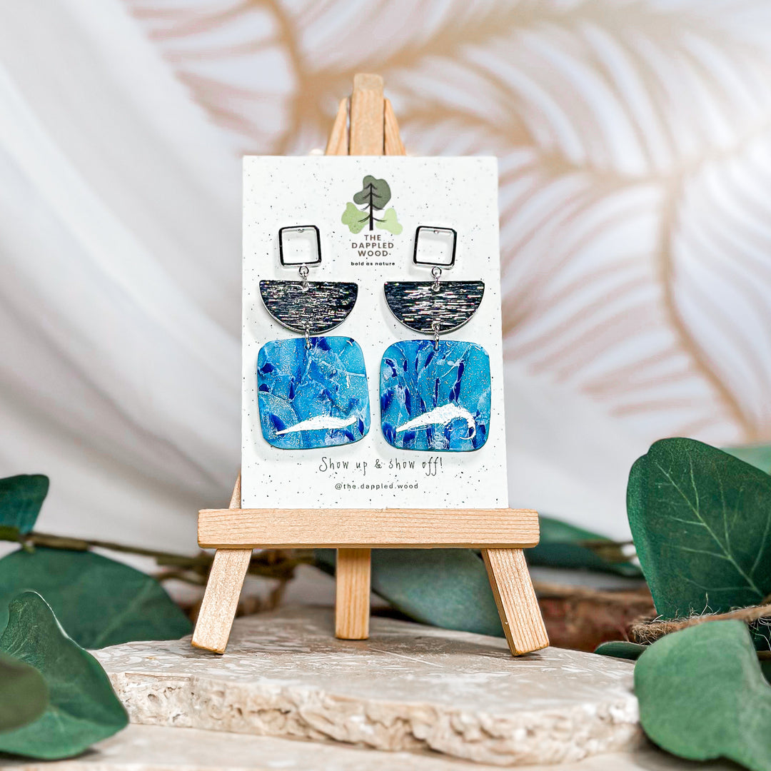 The Dappled Wood Oakley earrings from the Summer 2024 collection featuring a blue swirl polymer clay design, handmade and lightweight for sensitive ears.