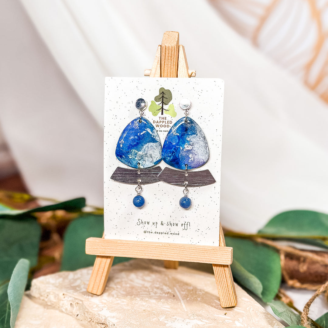 The Dappled Wood Oceania handmade polymer clay earrings from the Summer 2024 collection, featuring a blue, violet, and silver watercolor design for a bold statement while remaining lightweight and suitable for sensitive ears.