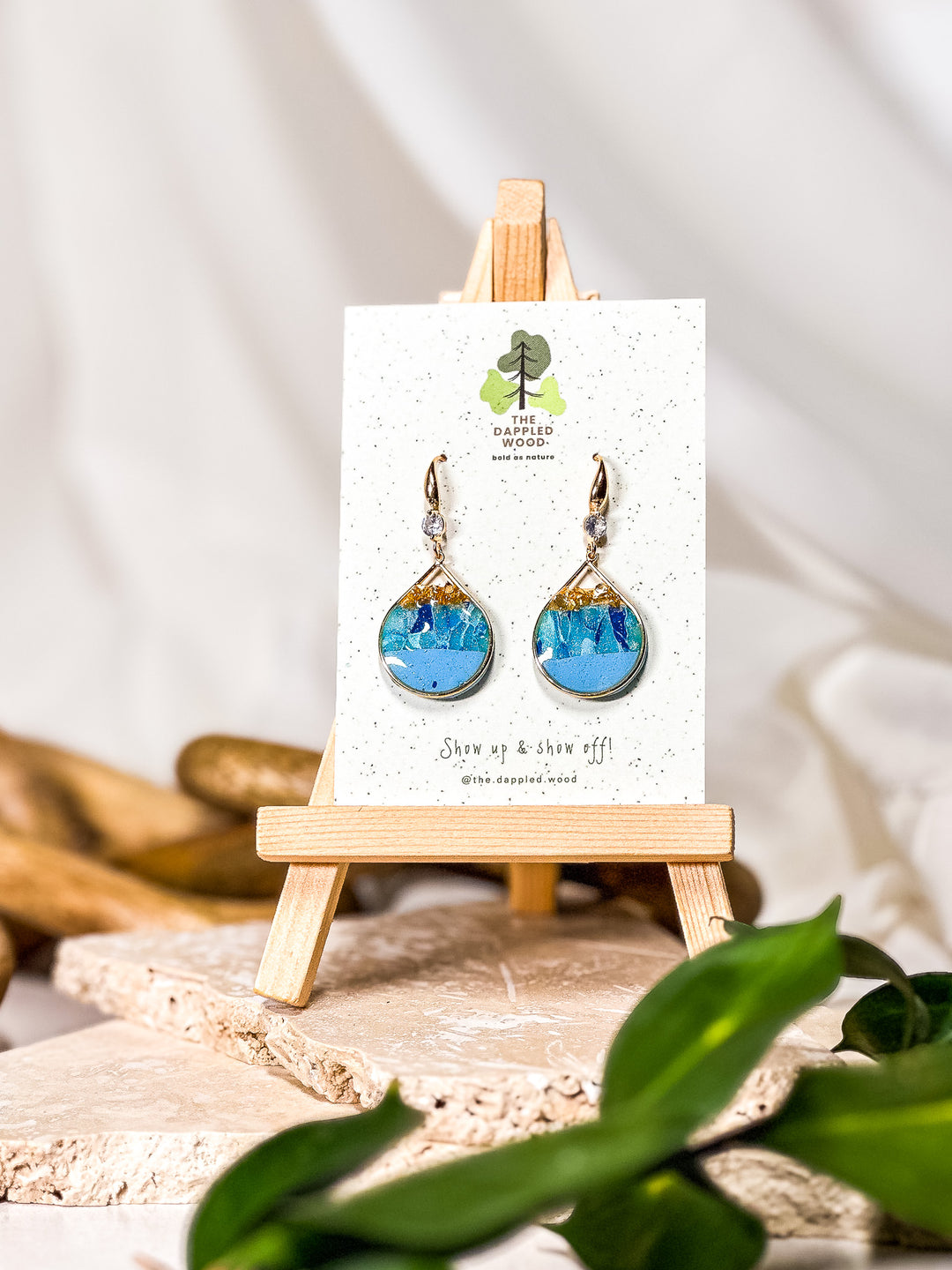 Light blue teardrop earrings framed in gold, featuring delicate gold glitter veining and set on a gold CZ hook. Inspired by the ocean hues of larimar earrings, part of The Dappled Wood's summer 2024 Poolside collection.