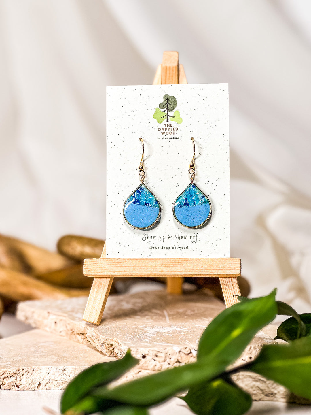 Elegant blue earrings with a gold-framed teardrop design, hanging from a 18K gold French hook. A sophisticated accessory resembling the calming aesthetic of larimar earrings. Part of The Dappled Wood's Poolside collection from Summer 2024.