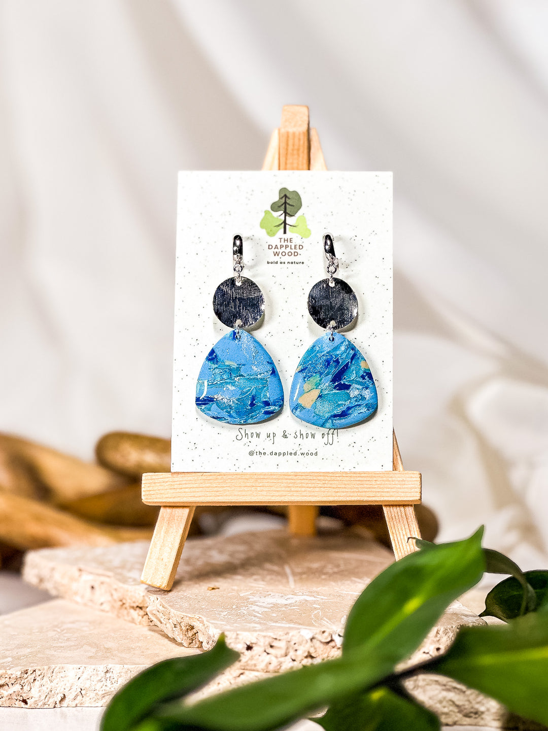 Blue earrings with a marbled effect, shaped like a guitar pick, suspended from a wavy textured circle connector on a silver hoop. A bold statement piece reminiscent of larimar earrings. Part of The Dappled Wood's Poolside collection from summer 2024.