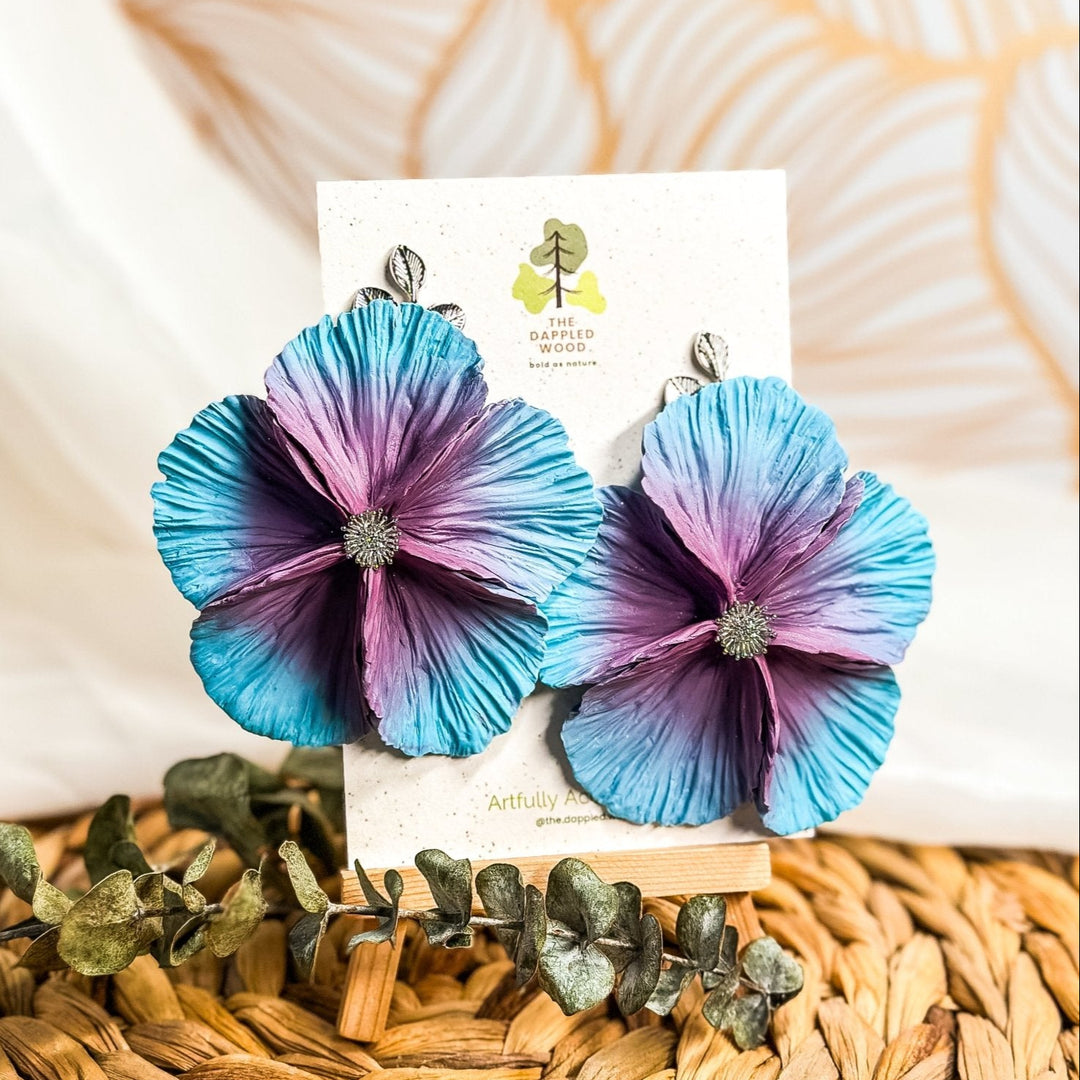 The Dappled Wood's Sabine polymer clay flower earrings in Starflower feature a lavender to sky blue gradient. Bold floral clay earrings and lightweight statement jewelry, perfect for garden parties or daytime celebrations.