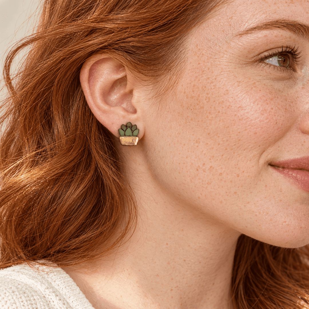 AI-generated styling preview of a model with auburn hair wearing a gold-pot Tansy succulent stud; scale is illustrative