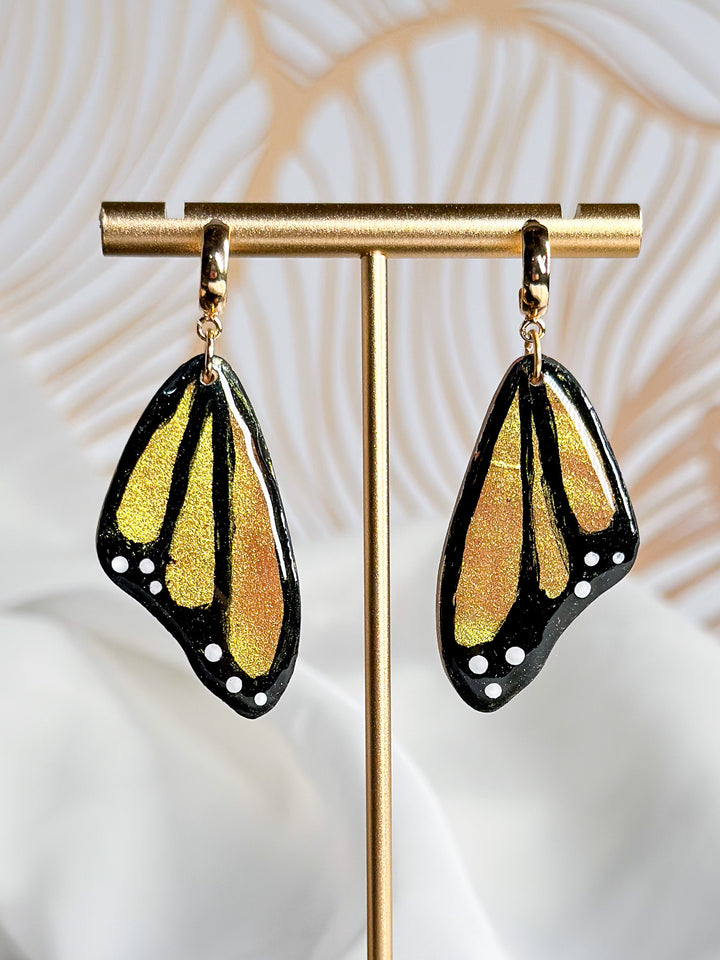 A close-up of The Dappled Wood’s Winged Whispers butterfly wing earrings in orange, featuring intricate nature-inspired details in a lightweight, hypoallergenic design.