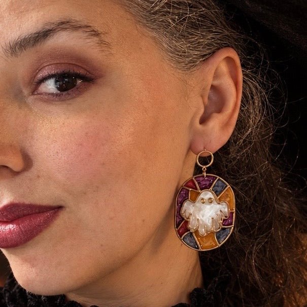 Close-up of a woman wearing Winifred stained glass ghost earrings in purple, red, blue, and gold.