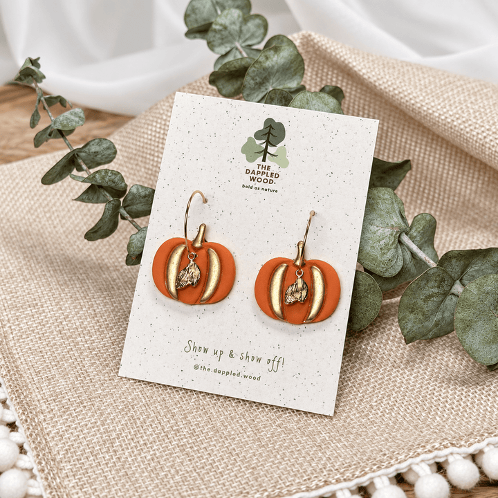 Winona gilded pumpkin earrings displayed with eucalyptus and natural woven textures.
