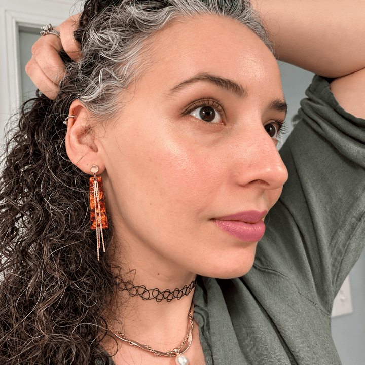 Woman wearing Ximena faux Mexican fire opal earrings with gold snake-chain tassels.