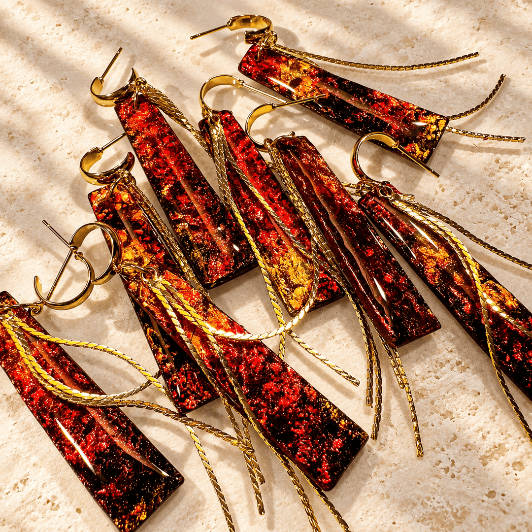 A collection of Ximena red, amber and gold faux fire opal tassel earrings arranged on warm ivory stone.