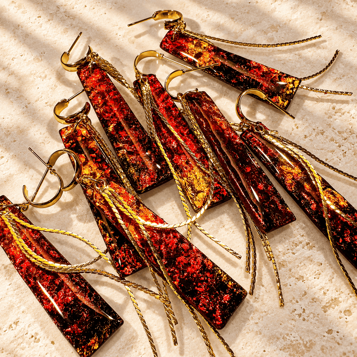 A collection of Ximena red, amber and gold faux fire opal tassel earrings arranged on warm ivory stone.
