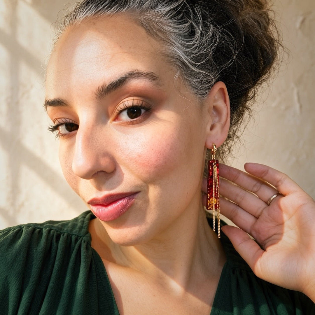 Model wearing Ximena red and gold faux fire opal tassel earrings with a forest green blouse.