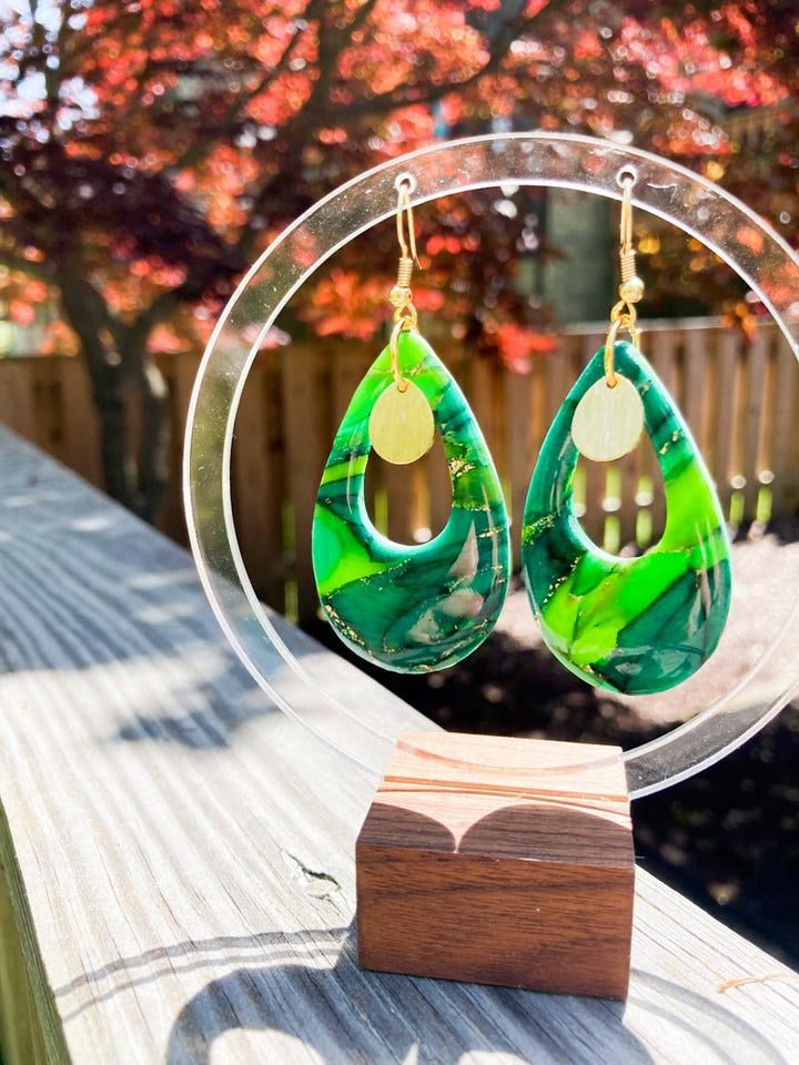 Esmeralda earrings displayed on a jewelry stand in natural lighting, showcasing their elegant teardrop shape, rich faux emerald marbling, and 18k gold-filled French hooks, a best-selling nature-inspired statement piece.