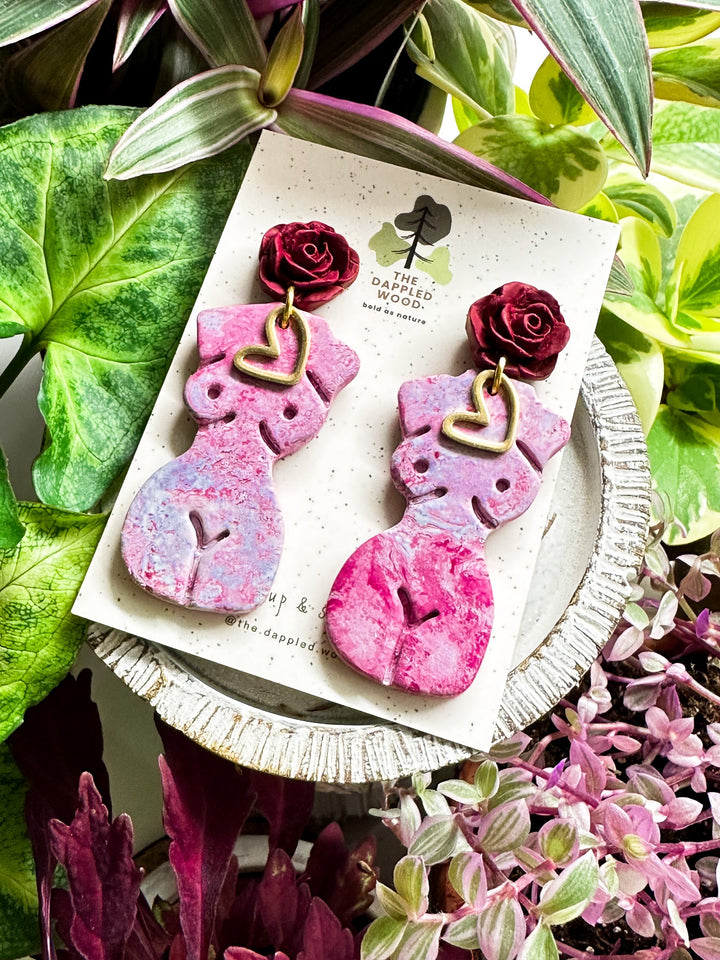 The Dappled Wood Frenchie earrings in Orchid. Marbled purple female figure statement earrings with soft pink floral details, handcrafted from polymer clay. Lightweight and hypoallergenic jewelry.